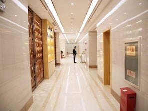 A hotel corridor with a polished floor, a reception area, and a person standing in the distance.