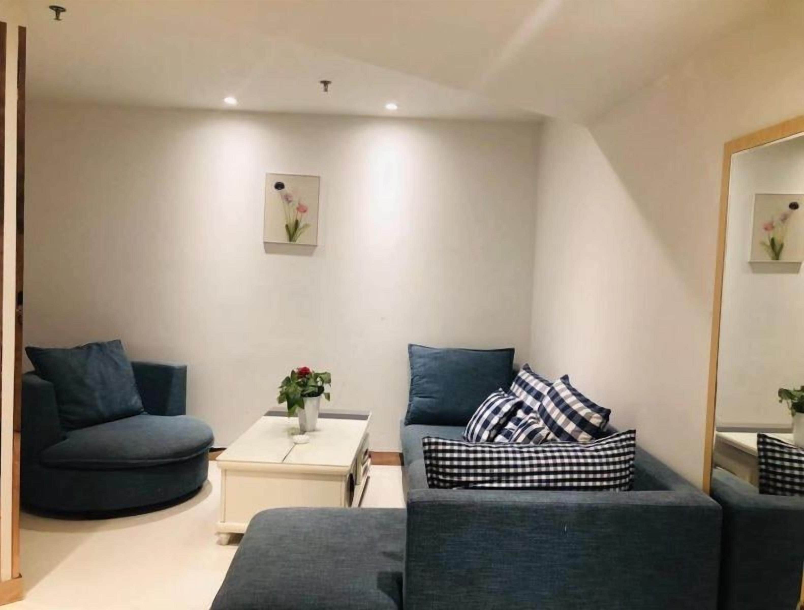 Una sala de estar moderna con un sofá azul oscuro, un sillón más pequeño y una mesita de noche blanca con un jarrón de flores.