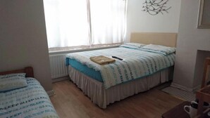 Un dormitorio con cama, mesita de noche, ventana con cortinas y radiador.