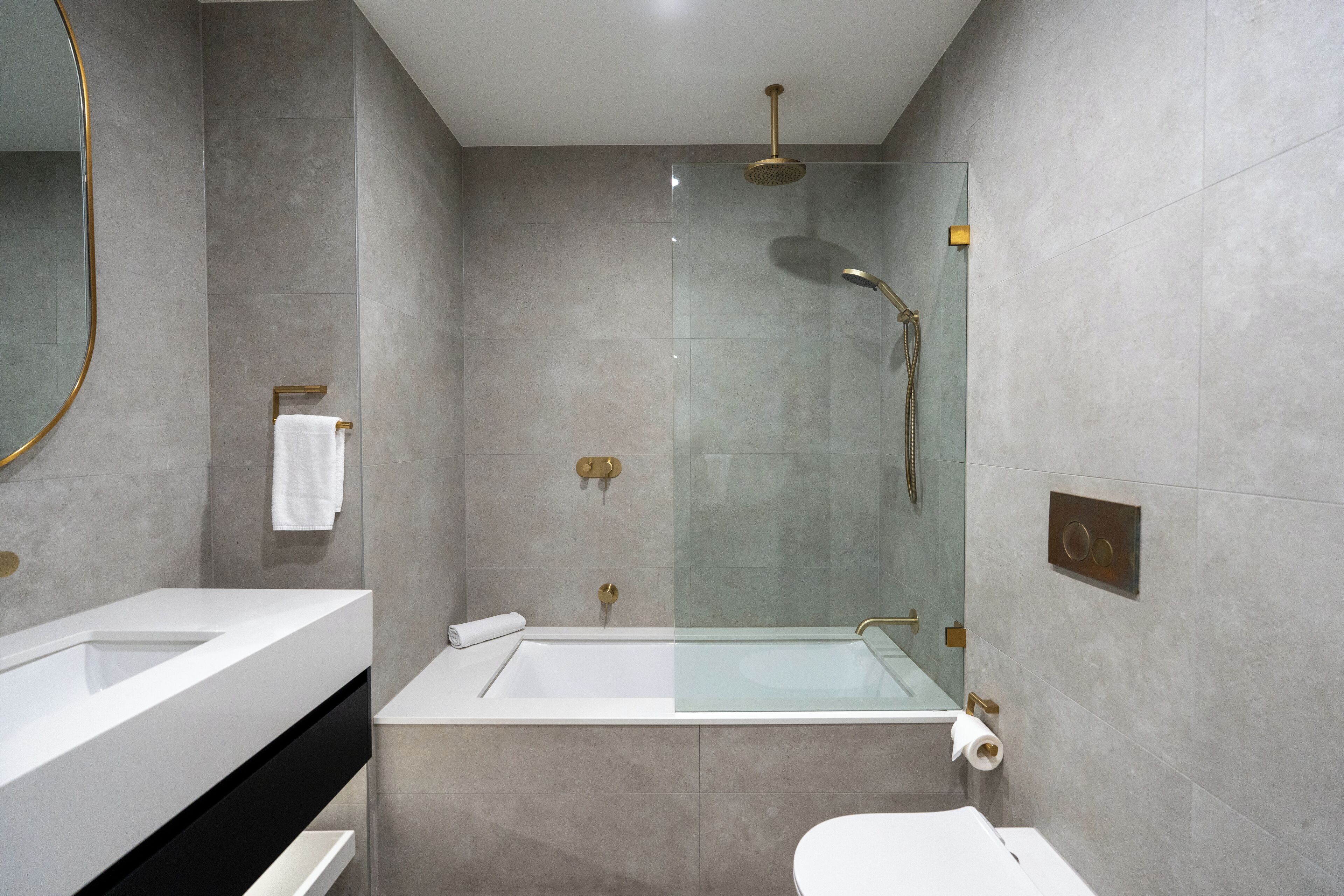 Een moderne badkamer met een glazen douchecabine, een wit bad en een apart toiletgedeelte.