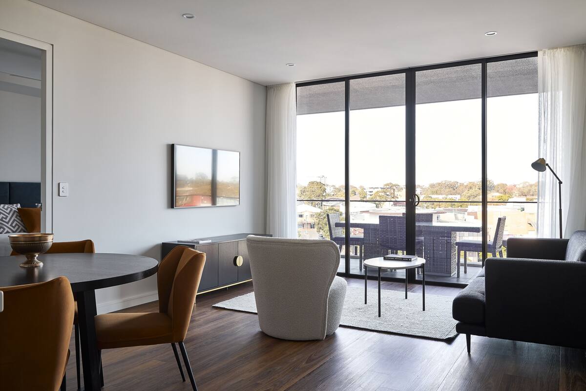 A modern living room with a dining area, large windows, and a view of the city.