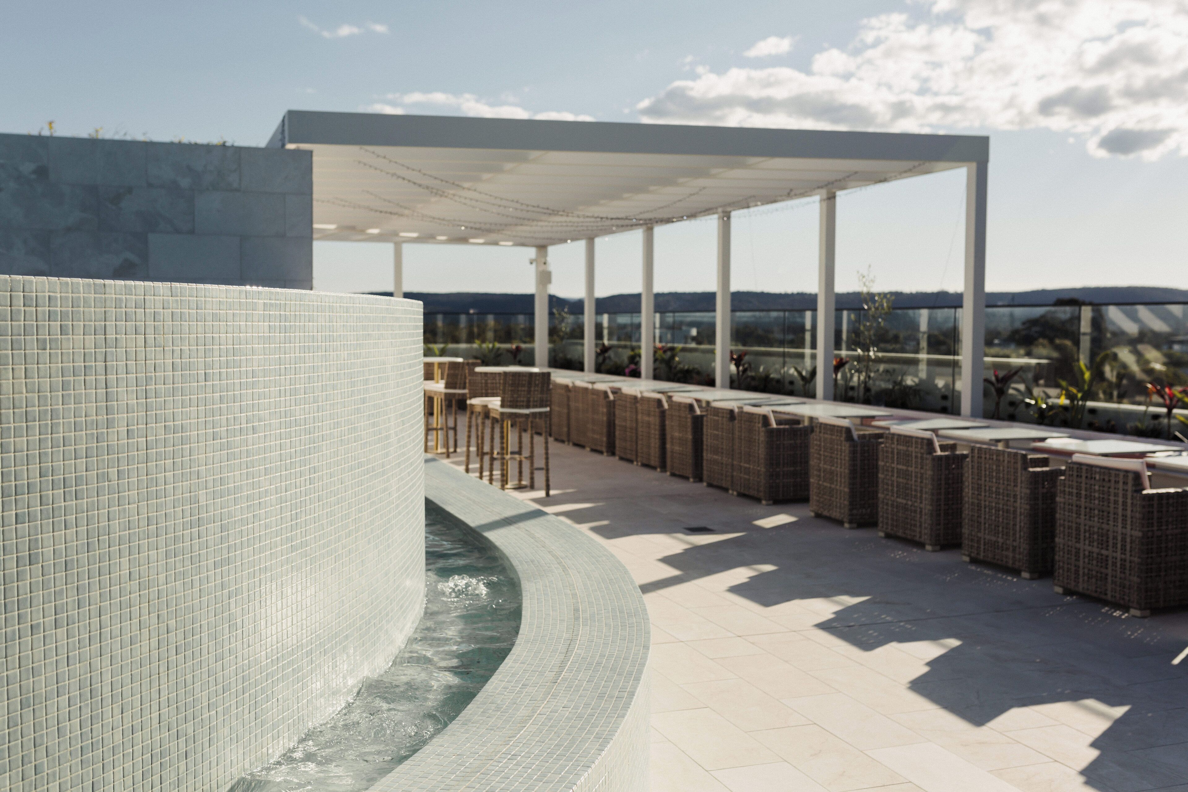 A rooftop terrace with a curved water feature, outdoor seating, and a view of the landscape.