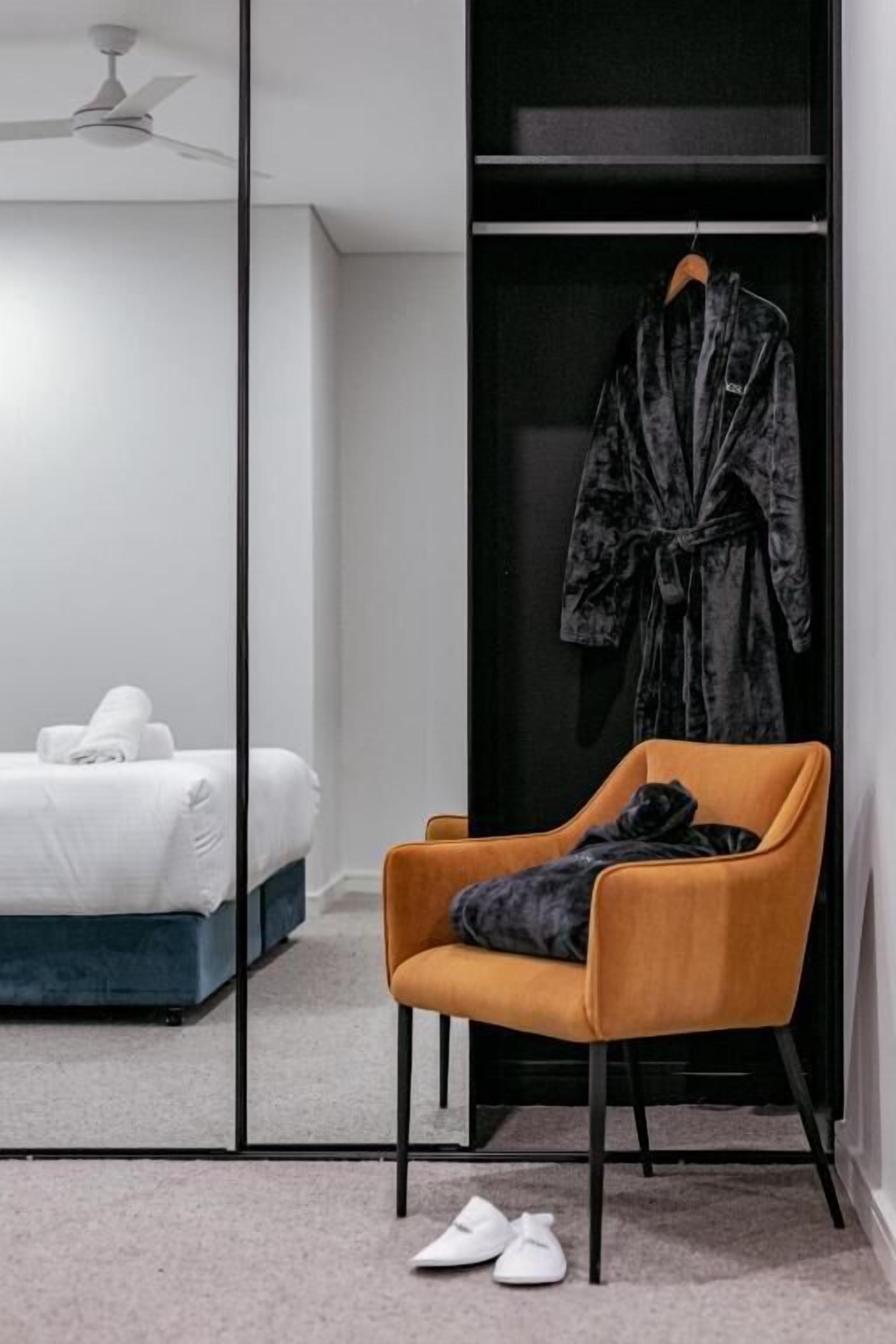 A bedroom with a bed, a chair, a robe hanging, and a pair of shoes on the floor.