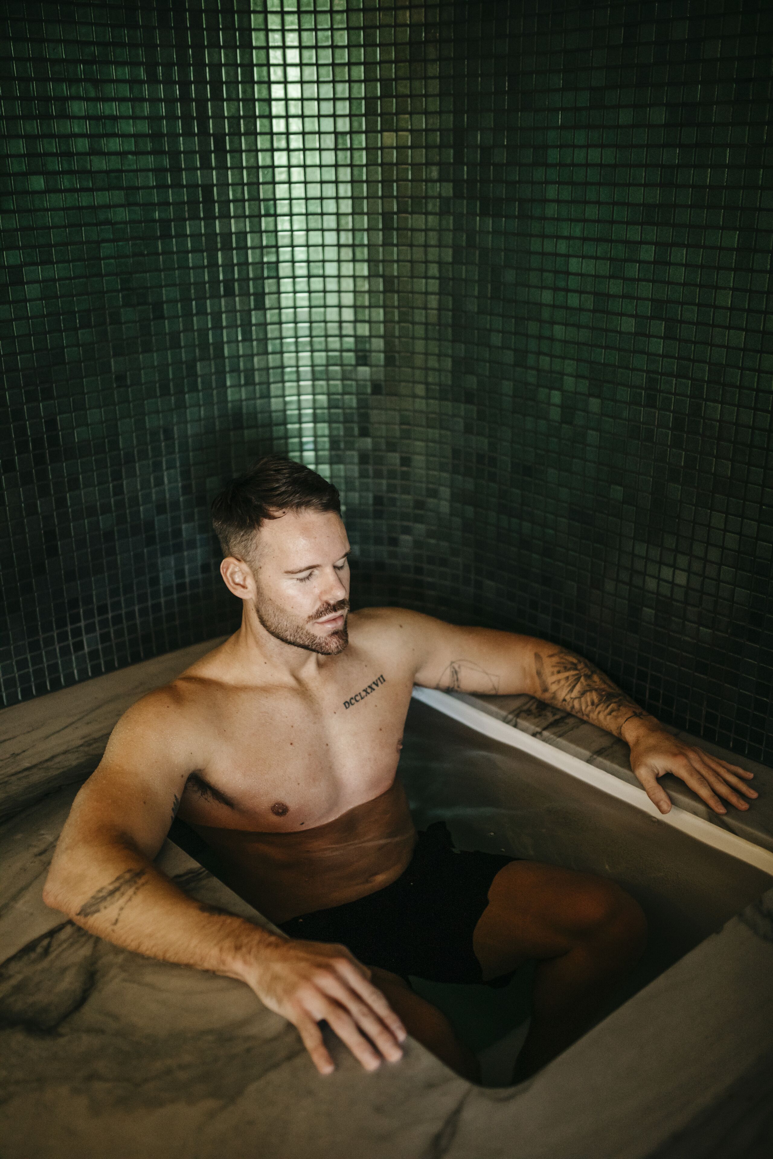 A man in a bathtub with tiled walls.