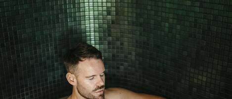 Ein Mann in einer Badewanne mit gefliesten Wänden.