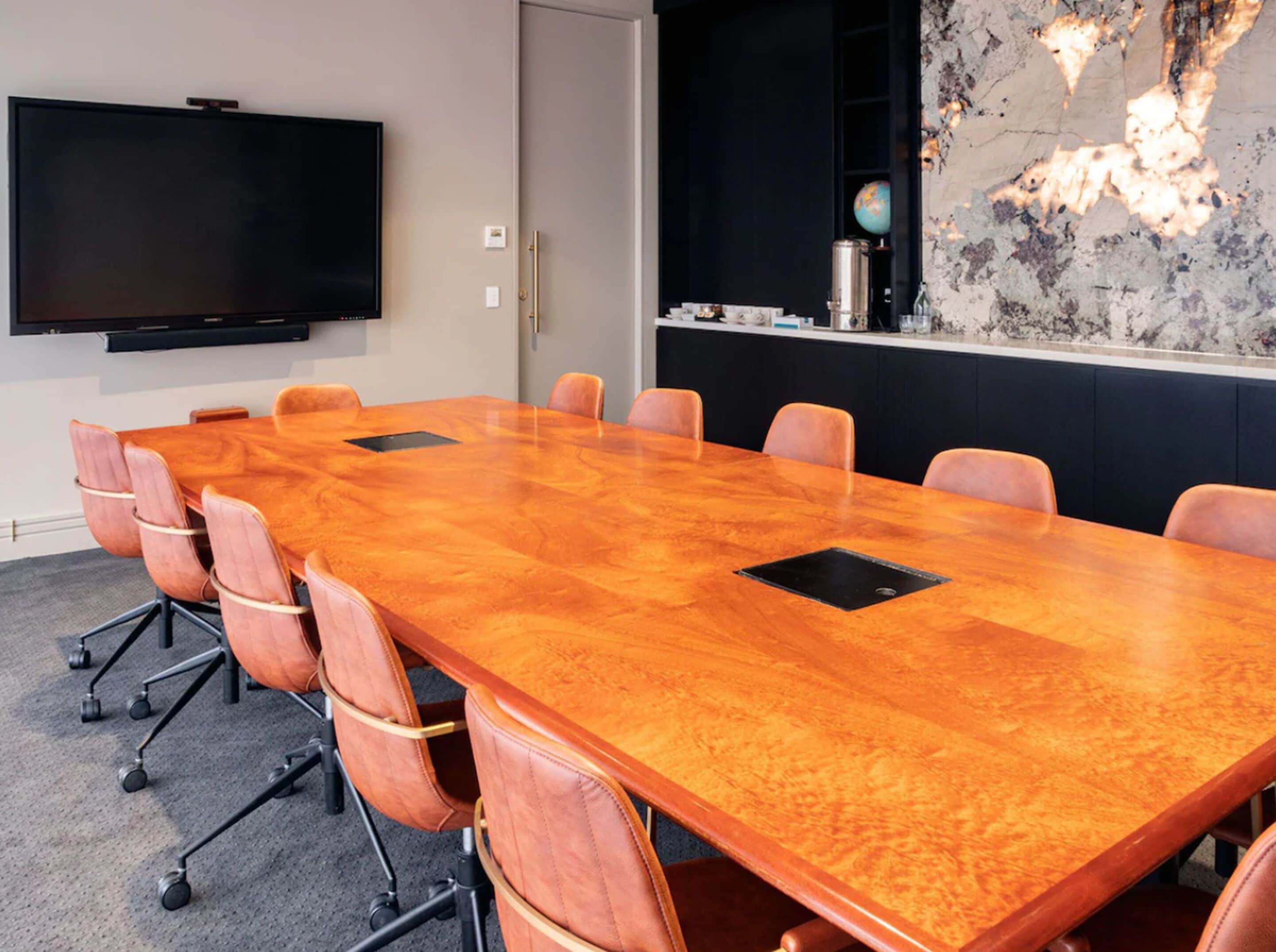 Une salle de conférence dotée d’une longue table en bois, de fauteuils en cuir, d’un téléviseur à écran plat et d’un mur décoratif orné d’un globe terrestre.