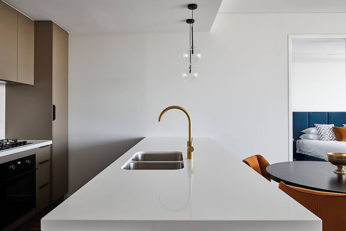 A modern kitchen with a white countertop, a gold faucet, and a built-in oven.