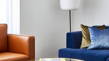 A modern living room with a leather armchair, a blue sofa, a glass coffee table, and a tall floor lamp.