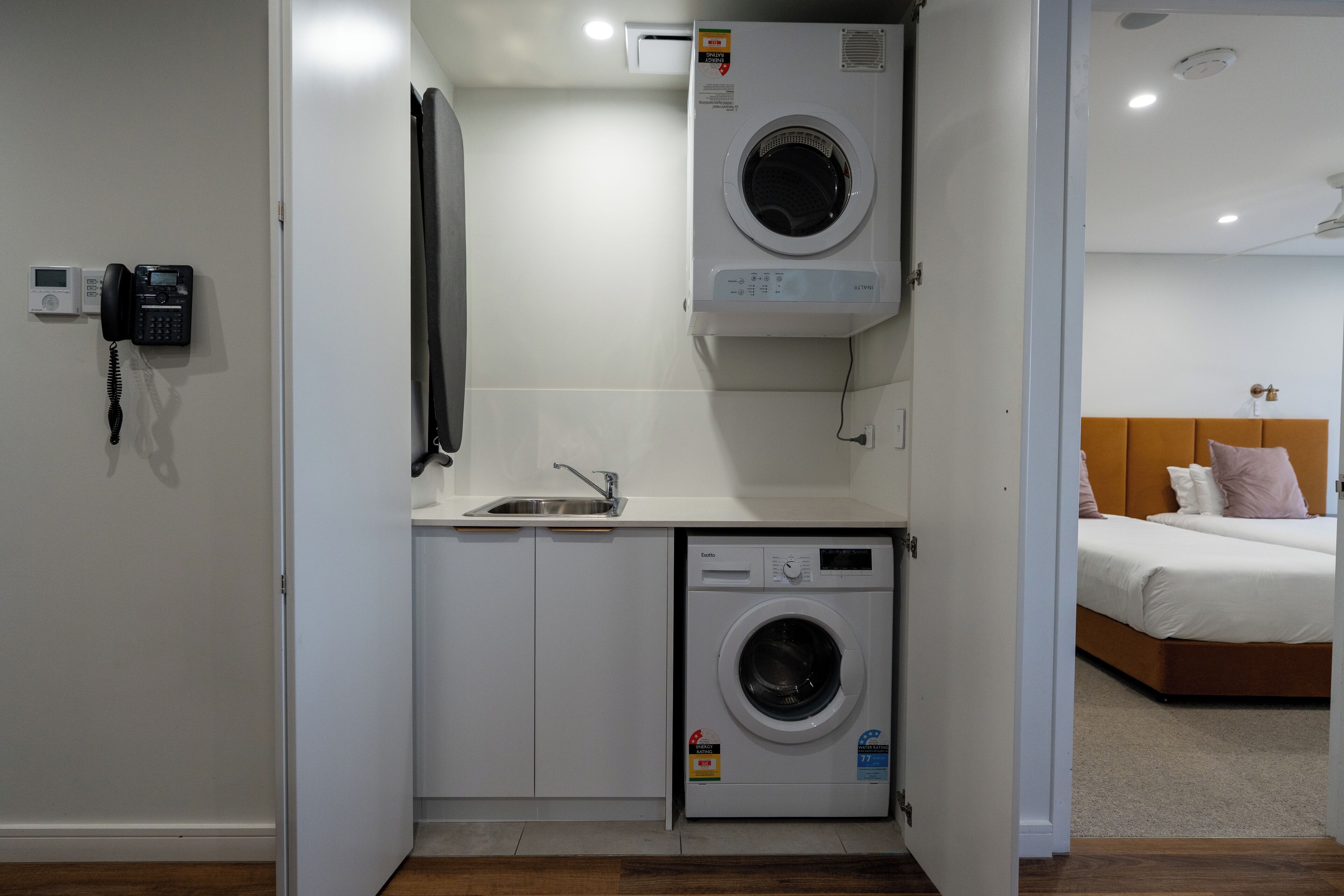 A compact laundry room with a washing machine, a sink, and a telephone.
