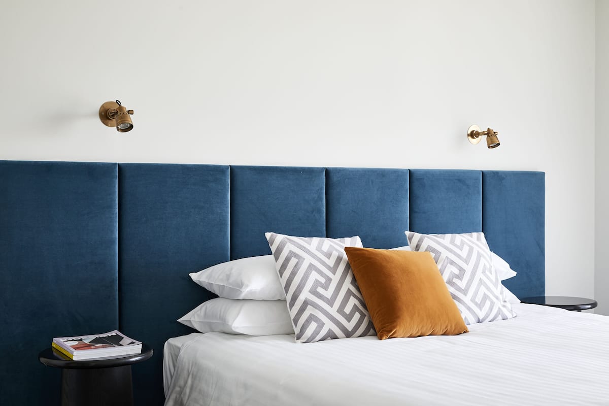 A bedroom with a blue upholstered headboard, white bedding, and patterned pillows.
