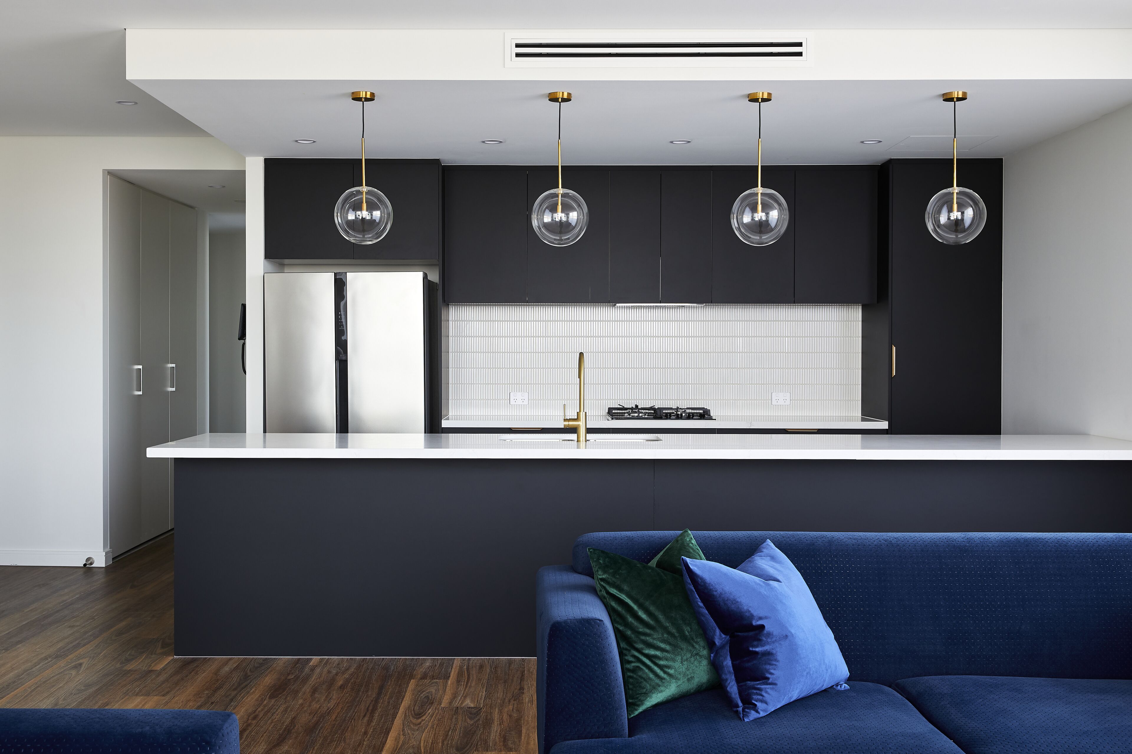 Uma cozinha moderna com ilha central, armários pretos e iluminação pendente.