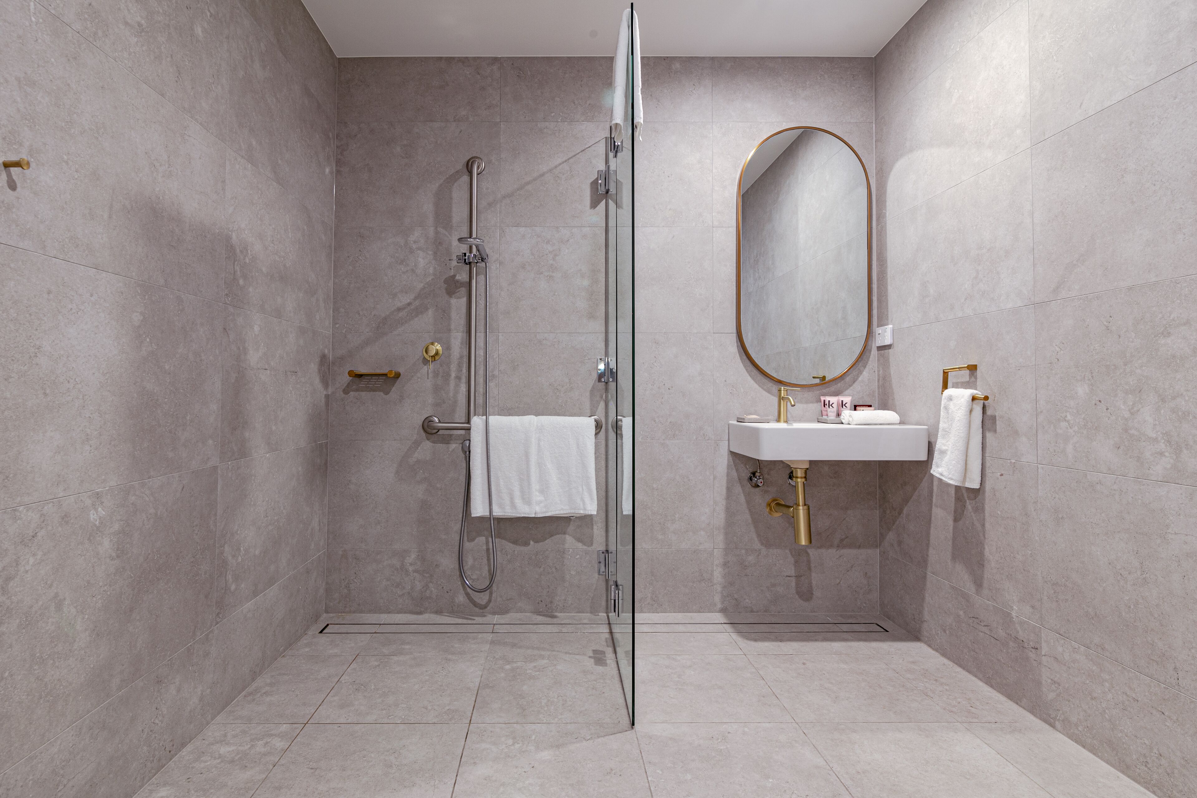 A modern bathroom with a glass shower enclosure, a white sink with gold fixtures, and a large mirror.