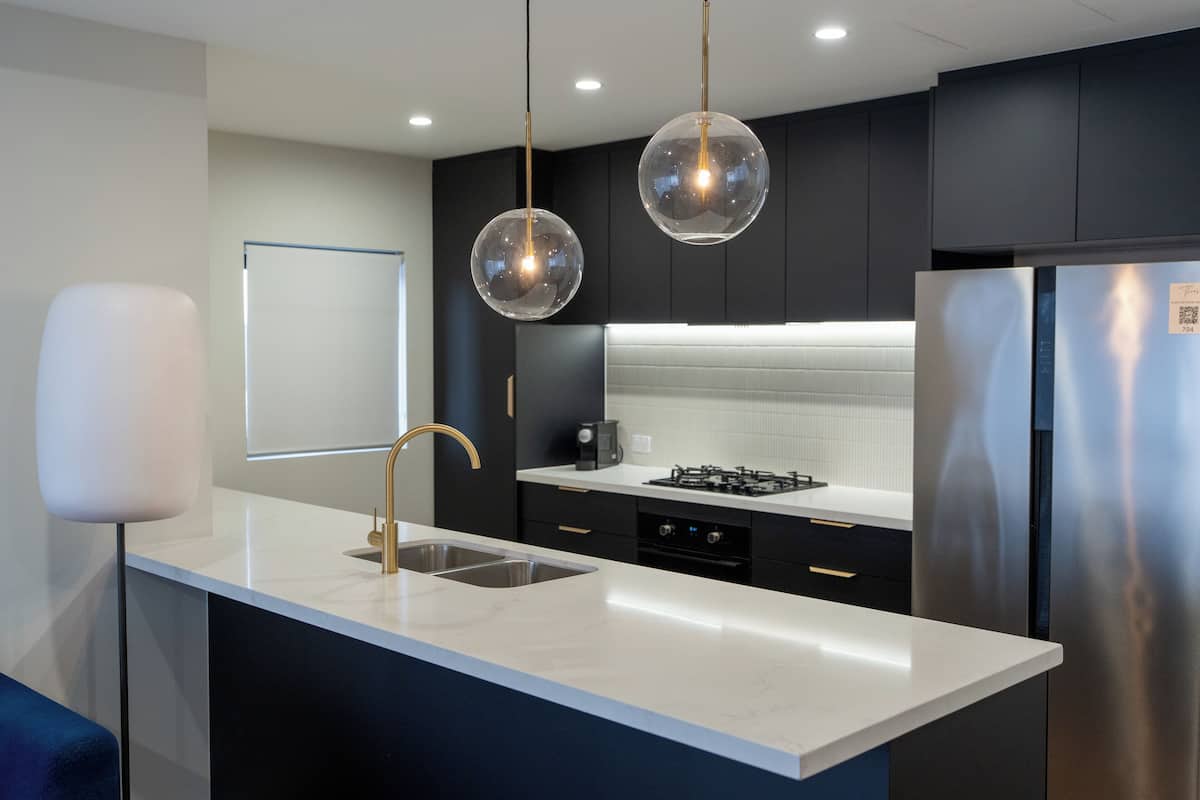 A modern kitchen with a white countertop, stainless steel appliances, and pendant lighting.
