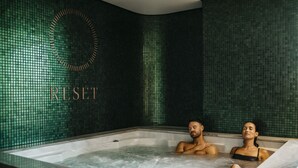 A spa room with a large bathtub, a wall with a green mosaic pattern, and the word "RESET" visible.