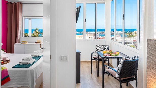 A modern hotel room with a balcony, a dining area with a table and chairs, and a view of the sea and marina. - Rosamar 313 Luxury sea view wifi (Arona)