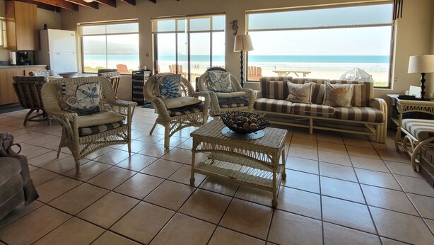A spacious living area with a high wooden ceiling, large windows offering a view of the beach, wicker furniture, and a tiled floor. - CASA MARBELLA 2BR/1BA Private Beach-Front Home (Ensenada)
