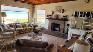 A cozy living room with wicker furniture, a fireplace, and a view of the outdoors. - CASA MARBELLA 2BR/1BA Private Beach-Front Home (Ensenada)