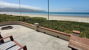 An outdoor patio with wooden benches and a concrete floor, overlooking a beach with a clear sky and distant mountains. - CASA MARBELLA 2BR/1BA Private Beach-Front Home (Ensenada)