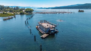 Una estructura flotante con terraza, una bandera y un muelle que se extiende sobre aguas tranquilas.