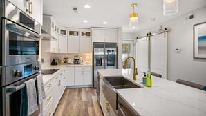A modern kitchen with white cabinetry, stainless steel appliances, and a marble countertop.
