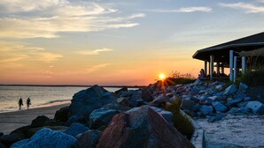 A beach with large rocks, a sunset, and a covered area with people.