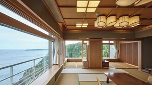 Een ruime kamer met een grote houten tafel, tatami matten en uitzicht op zee.