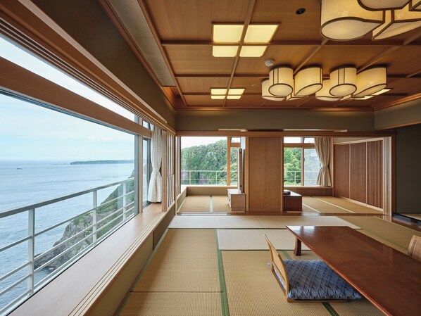 Una habitación amplia con una gran mesa de madera, esteras de tatami y vistas al mar.
