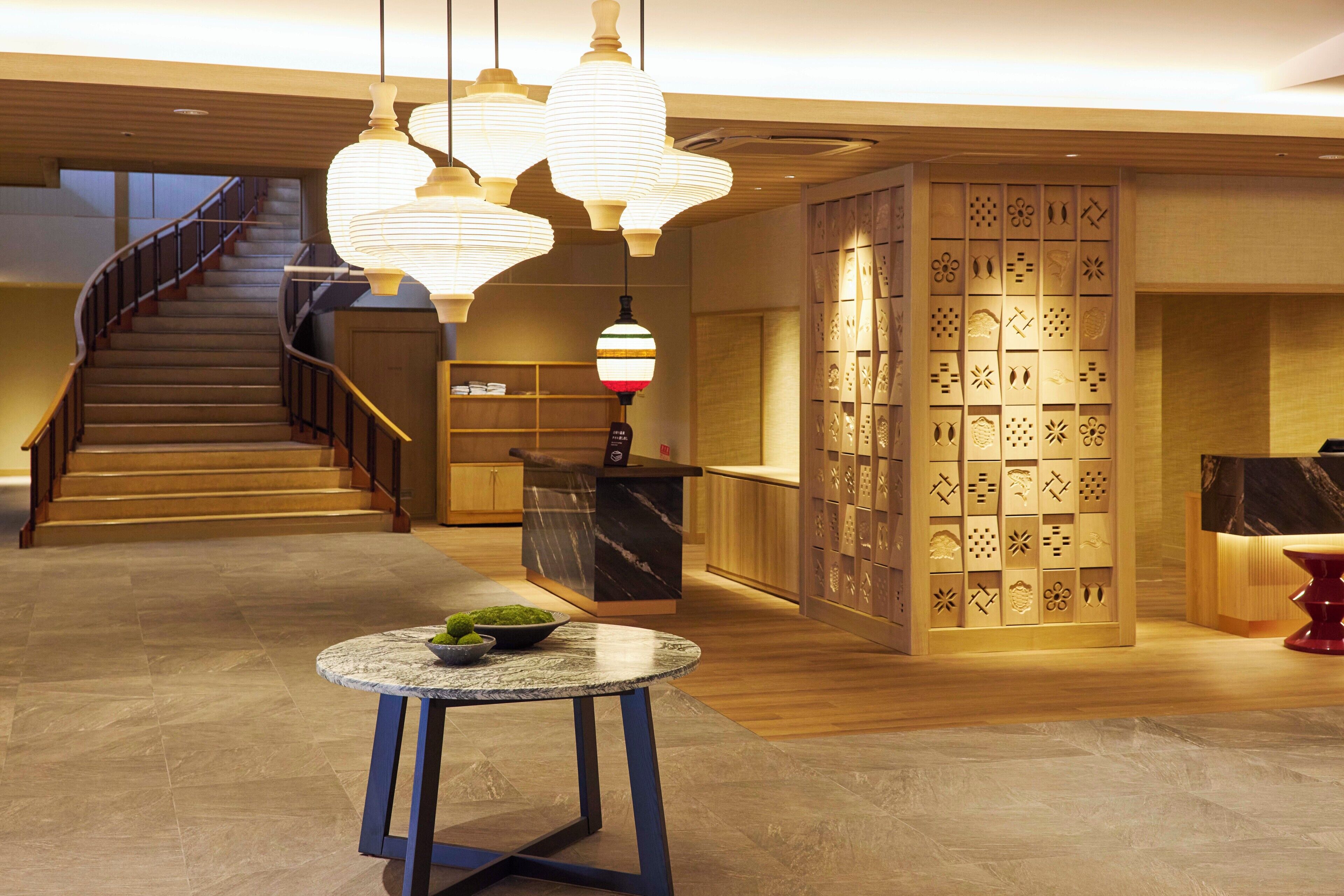 Un vestíbulo de hotel con una escalera, un mostrador de recepción y una pared decorativa con diseños recortados.