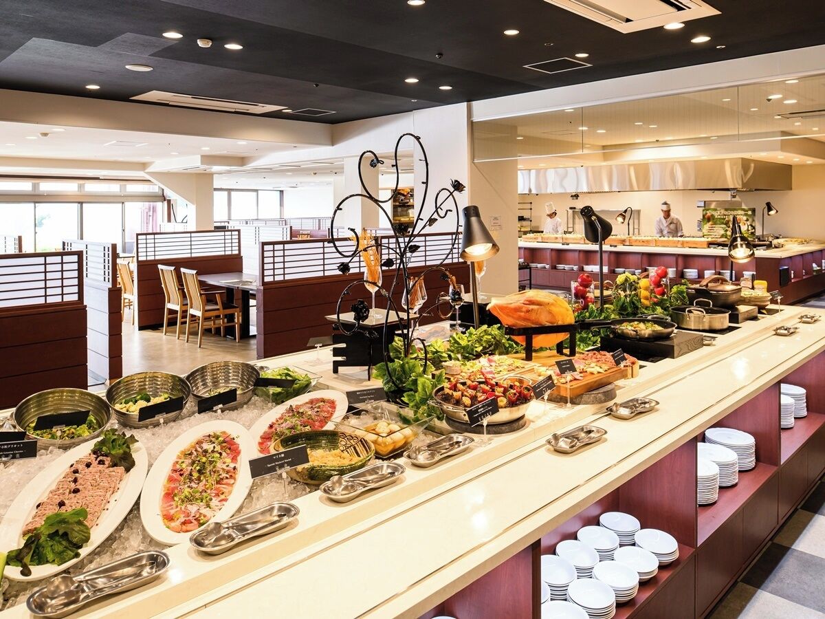 A buffet with various food stations, a seating area with tables and chairs, and a kitchen area in the background.