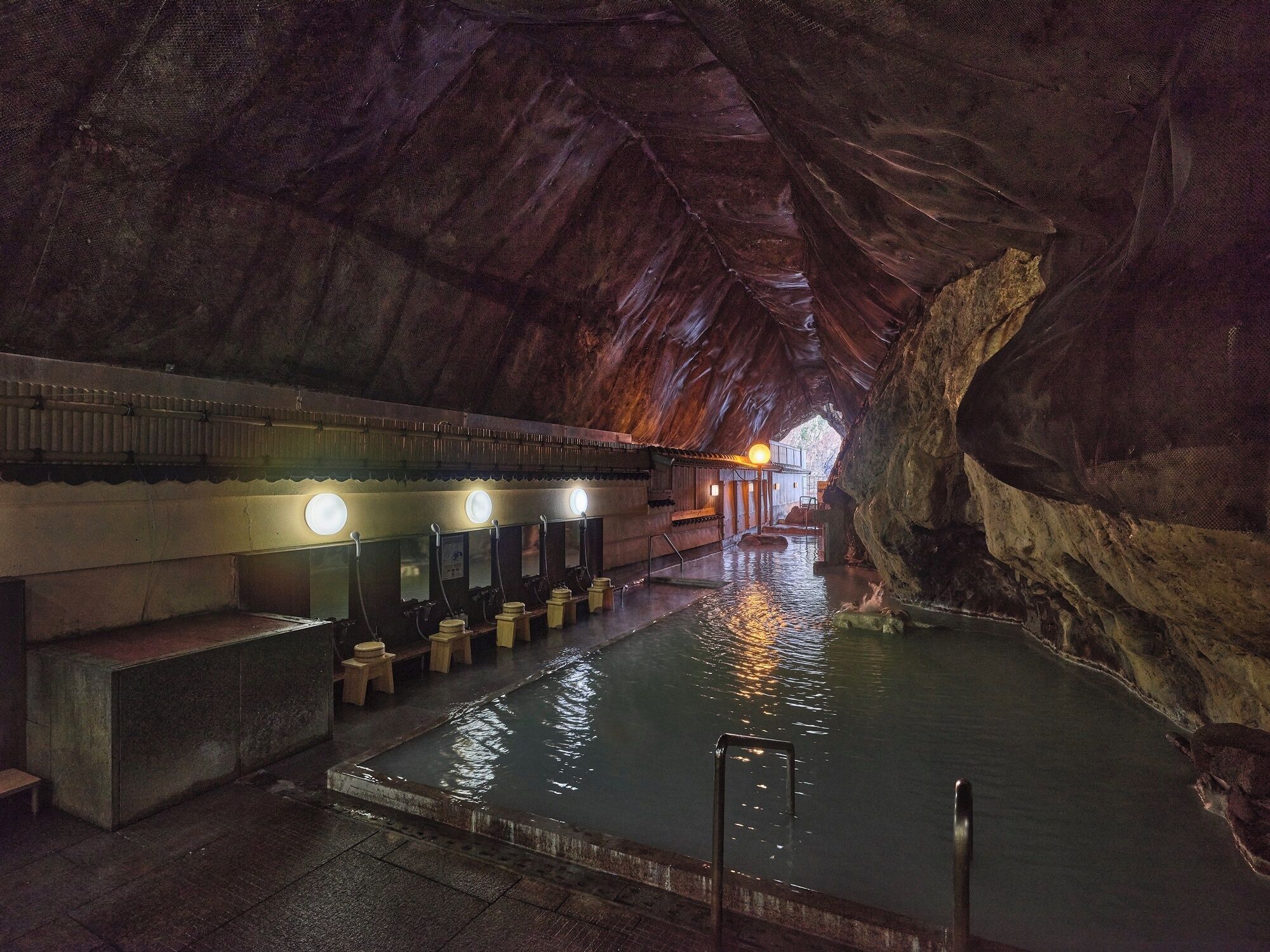 A cave-like structure with a pool, benches, and a row of sinks with lights.