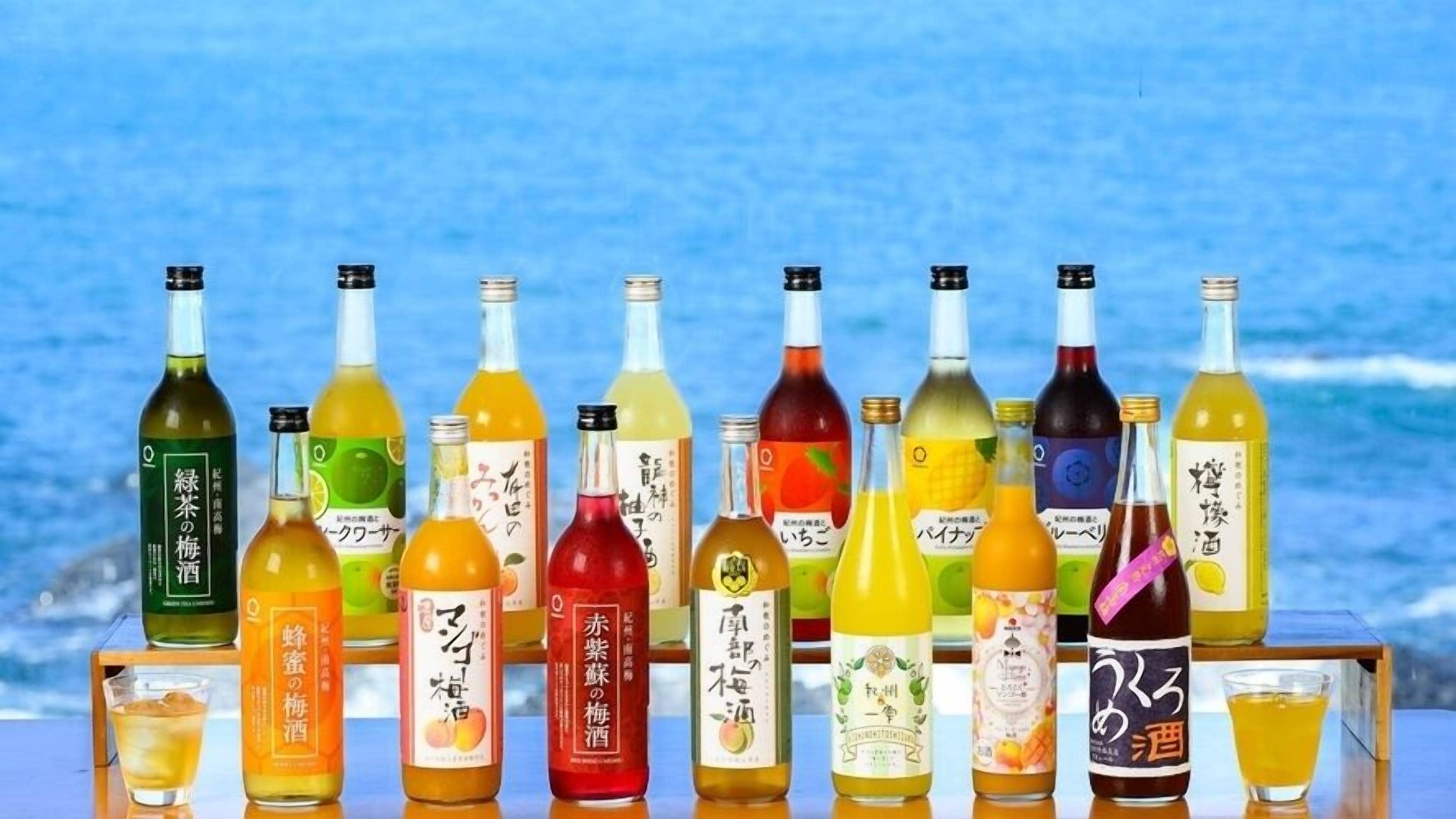 A variety of bottles with Japanese labels, arranged on a table with a view of the sea in the background.