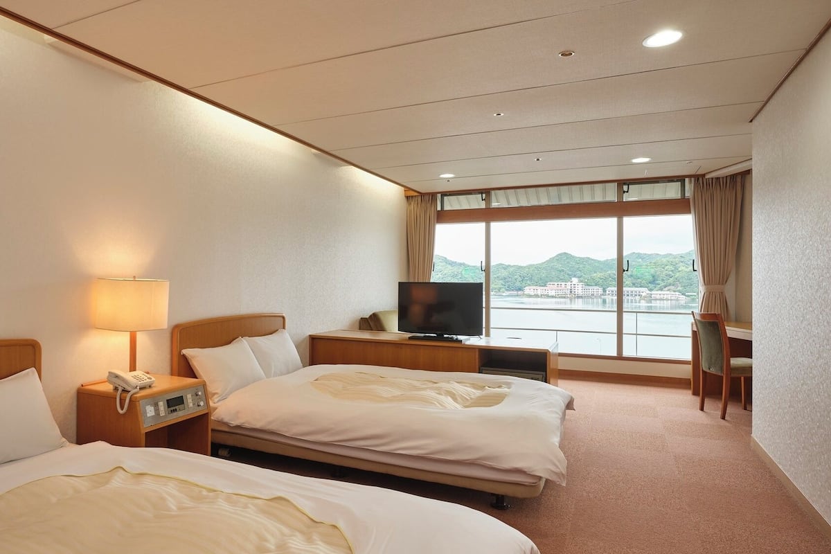 Une chambre d’hôtel avec deux lits, une télévision, un bureau et une fenêtre donnant sur un plan d’eau.