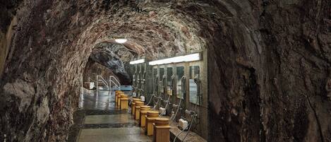 A tunnel with a wet floor, stone walls, and multiple sinks along the sides.