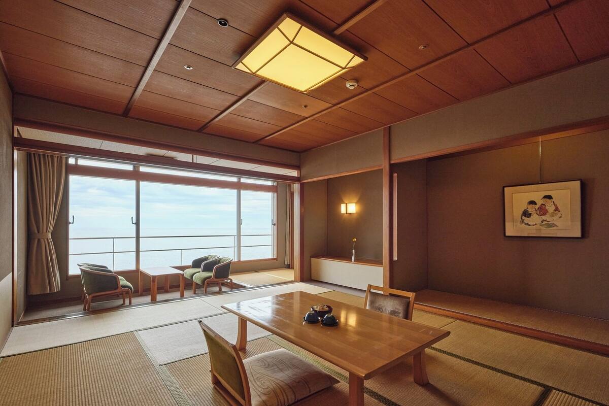 Une pièce de style japonais traditionnel, avec un sol recouvert de tatamis, une petite table en bois et une grande fenêtre donnant sur la mer.