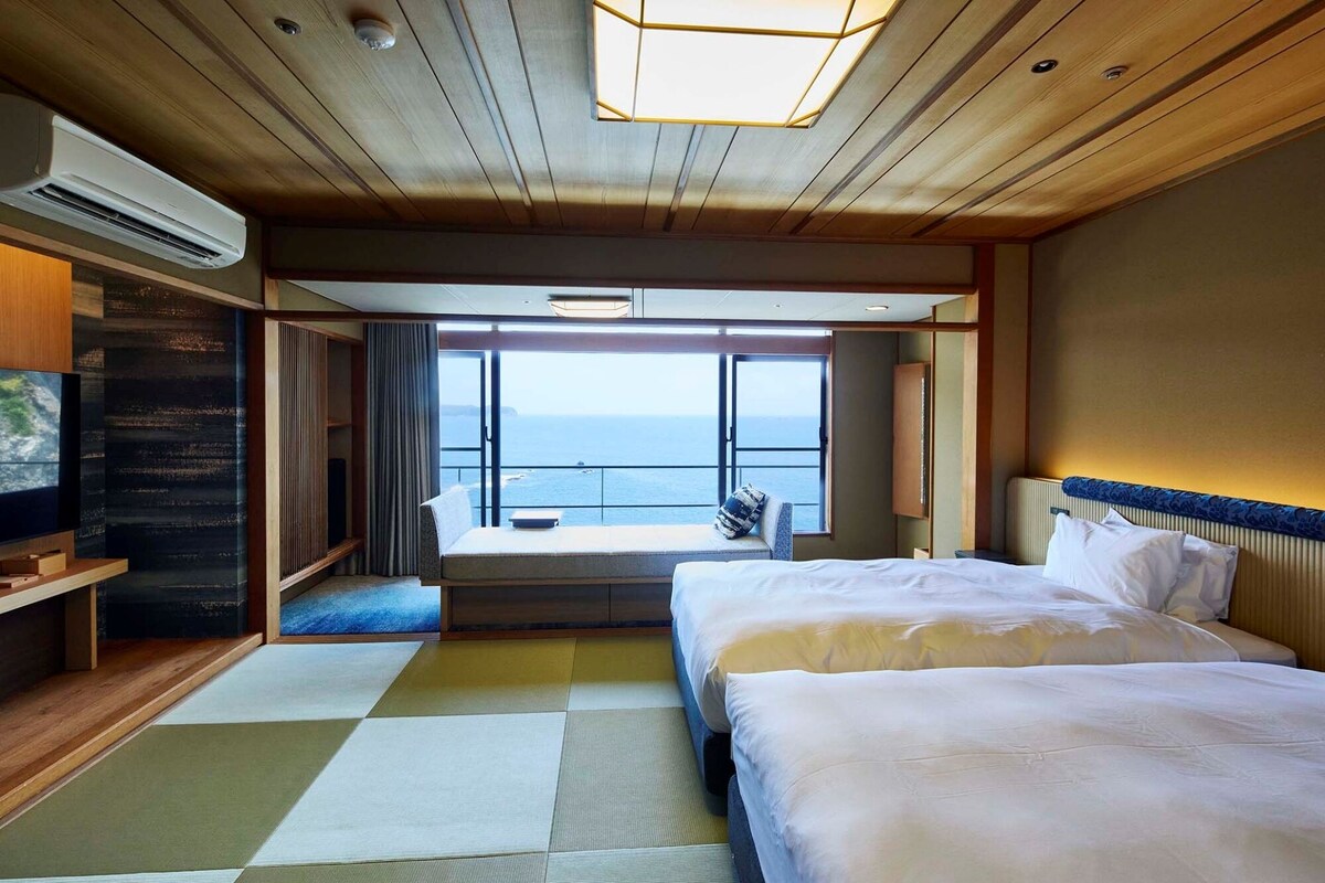 Ein Hotelzimmer mit Bett, Fernseher, einer Sitzecke mit Blick und einem großen Fenster.