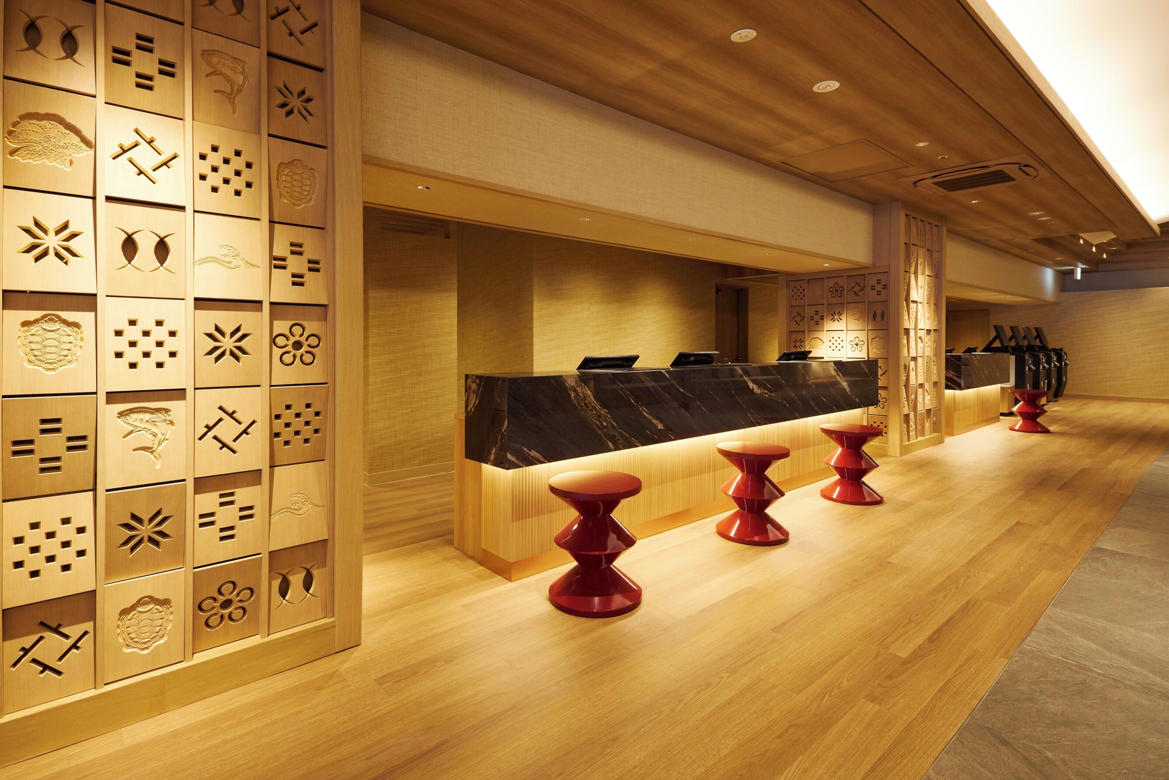 A hotel reception area with a wooden panel wall, a marble counter, and red stools.