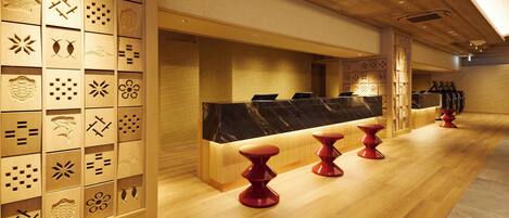 A hotel reception area with a wooden panel wall, a marble counter, and red stools.