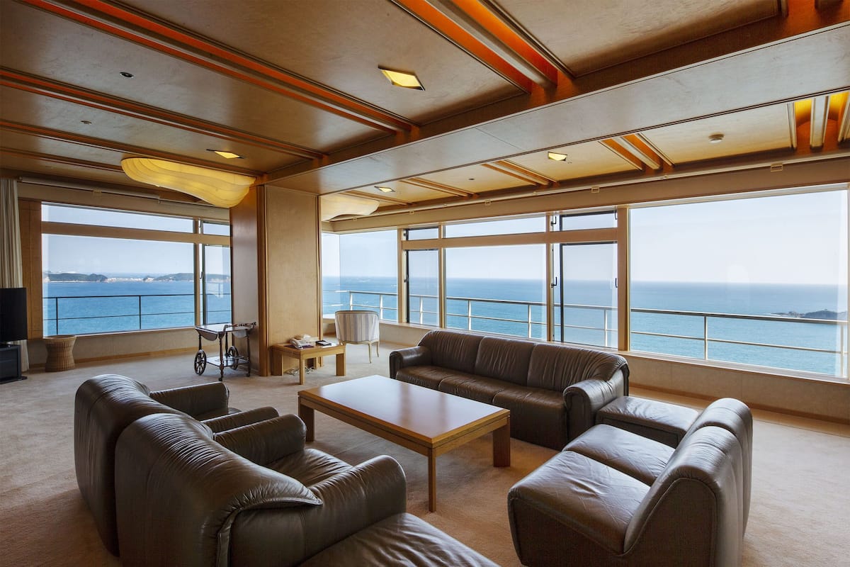 Un vaste espace de vie agrémenté de canapés en cuir, d’une table basse en bois et de grandes fenêtres offrant une vue sur la mer.