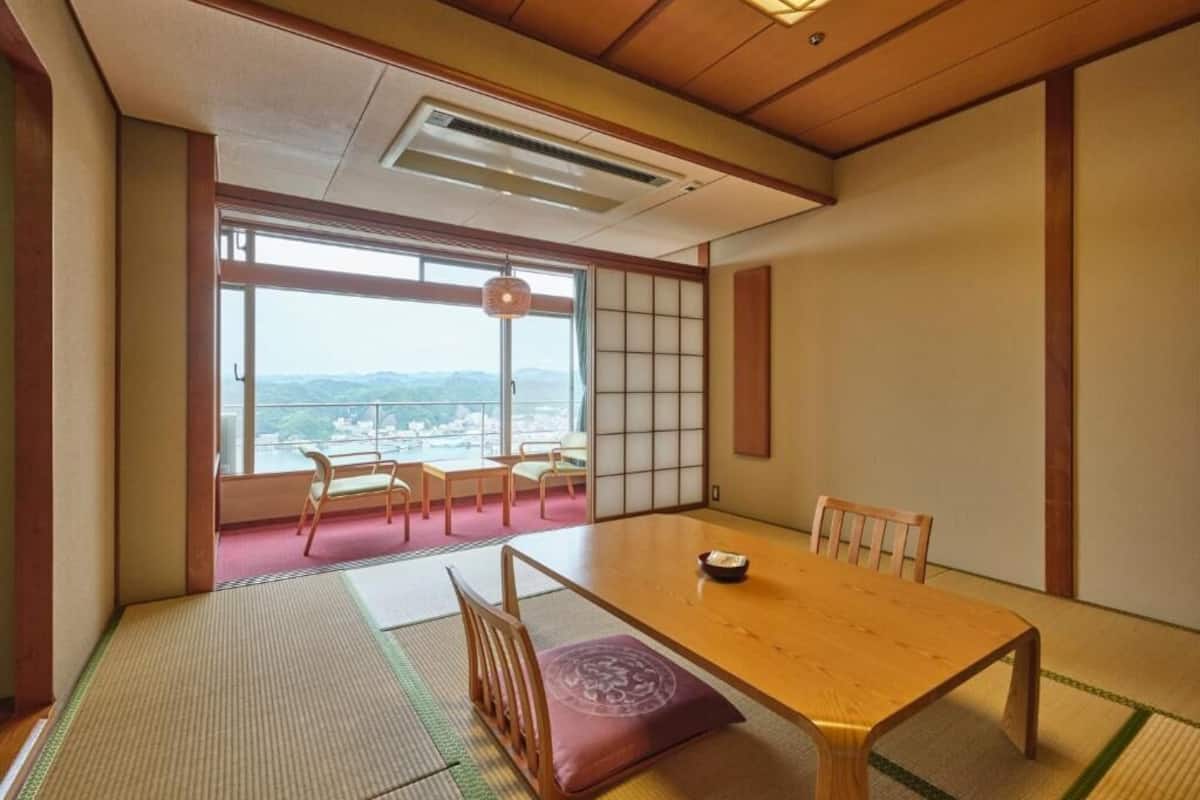 Une pièce de style japonais traditionnel, avec un sol recouvert de tatamis, une table en bois et une vue sur le paysage urbain à travers de grandes fenêtres.