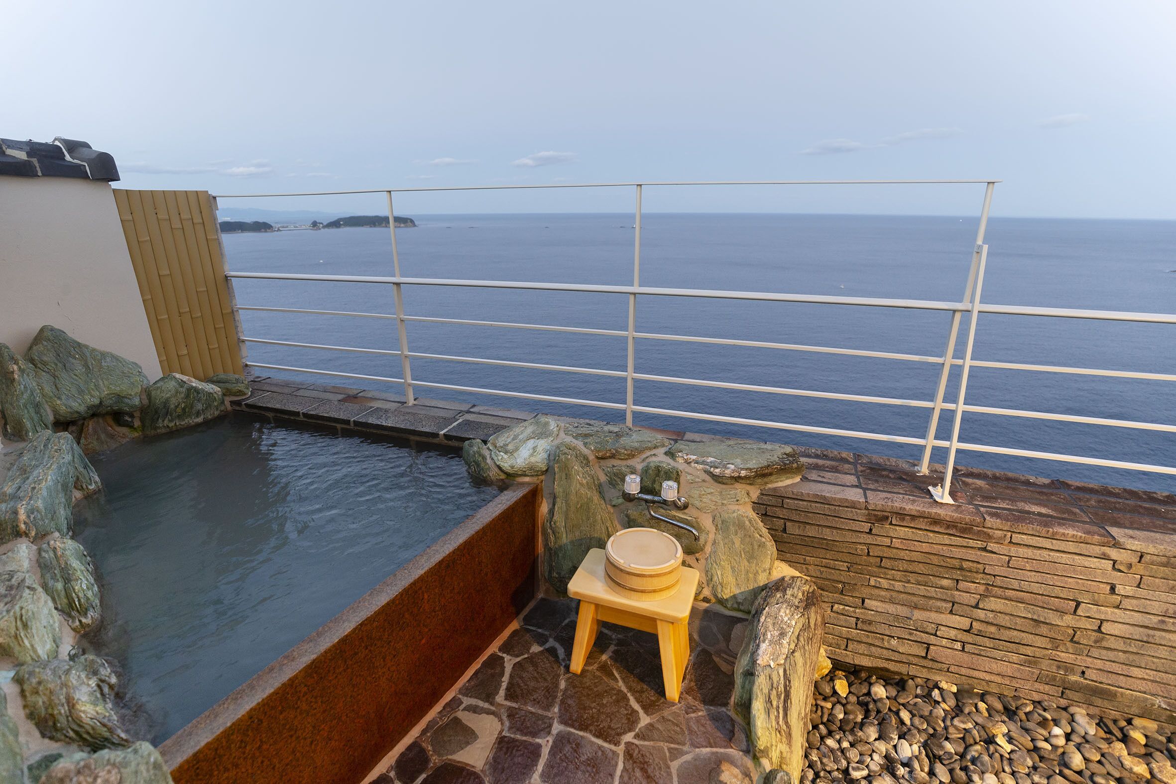 Ein Thermalbereich mit Blick auf das Meer, ein hölzerner Hocker und eine Steinmauer.
