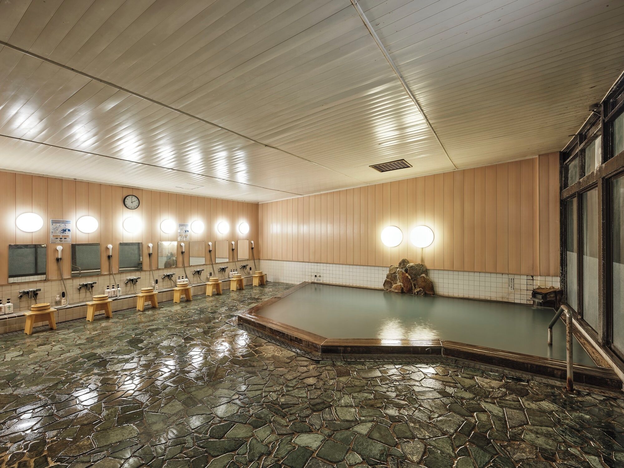 A spacious indoor swimming pool with stone flooring, wooden walls, and multiple benches.