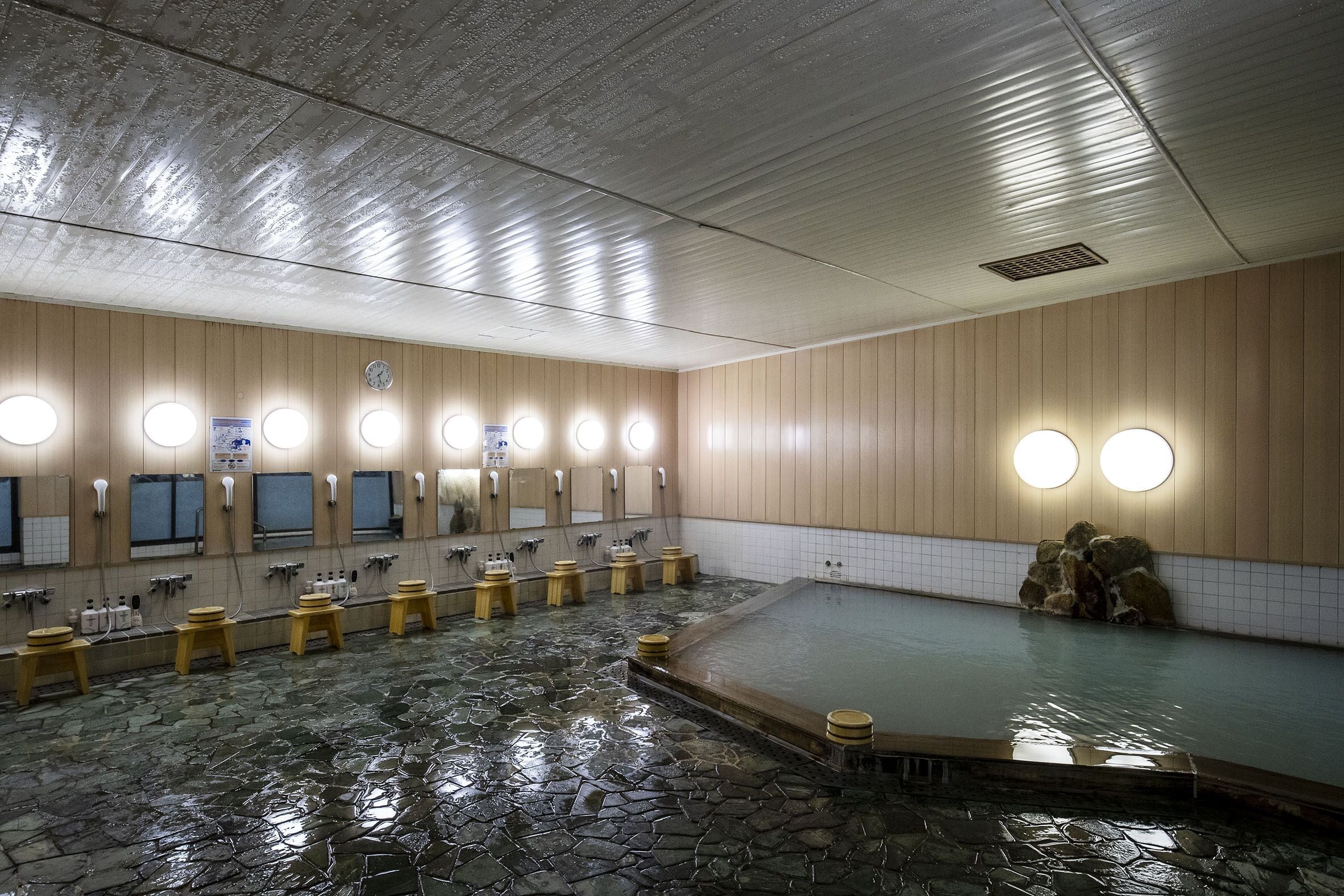 Ein traditionelles japanisches Onsen mit Steinböden, mehreren Waschtischen und einem Thermalbadbereich.
