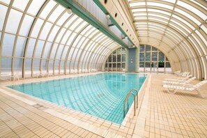 An indoor swimming pool with a curved glass ceiling, tiled floor, and lounge chairs along the perimeter. - Hotel Urashima (Nachikatsuura)
