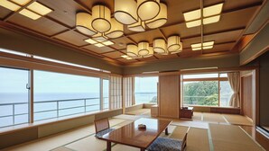 Een traditionele Japanse kamer met tatami vloeren, een lage tafel en schuifdeuren die uitkomen op een balkon met uitzicht op zee.