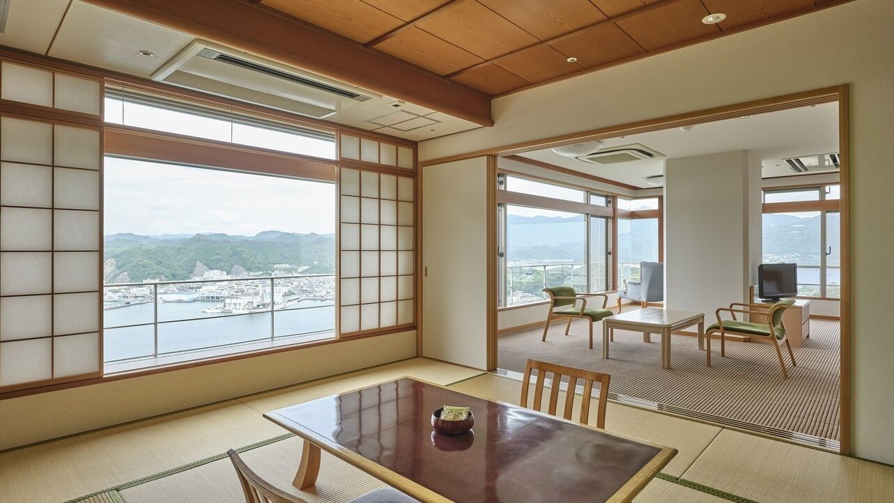 A traditional Japanese room with tatami flooring, a low table, and a view of a cityscape through large windows.