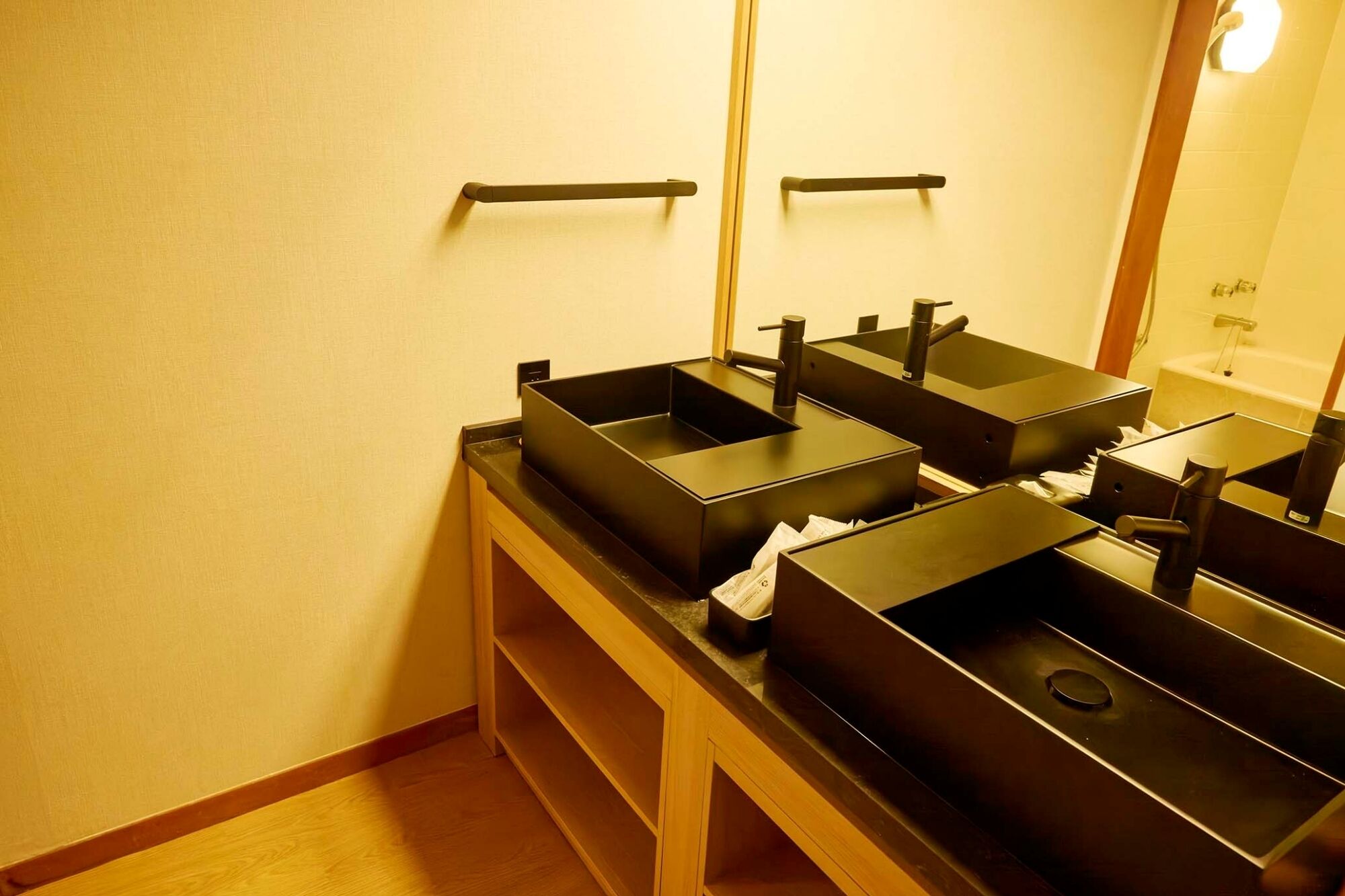 Une salle de bain avec deux lavabos noirs, un miroir et un meuble-lavabo en bois.