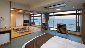Hotelkamer met een groot bed, een bureau, een stoel, een kleine tafel en uitzicht op zee.