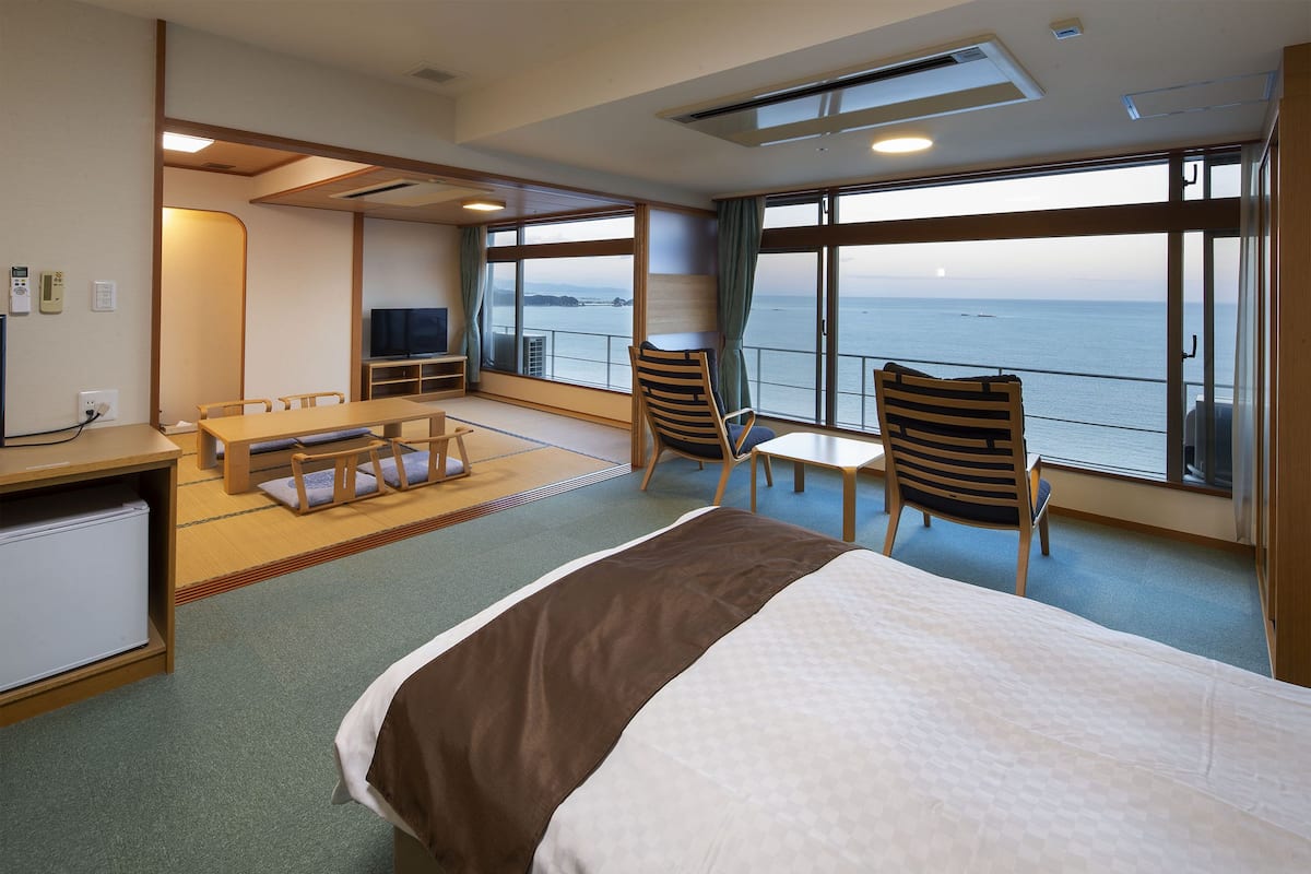 Une chambre d’hôtel avec un grand lit, un bureau, une chaise, une petite table et une vue sur la mer.