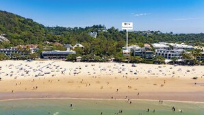 A beach with numerous umbrellas and people, a sign for 'Luxurystays', and buildings in the background.