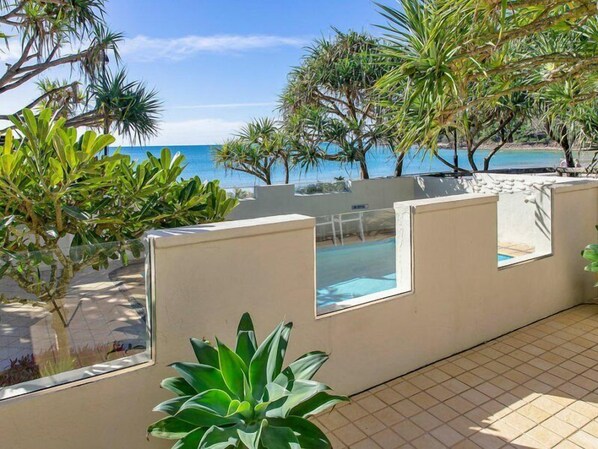 Un área de piscina con vistas despejadas al mar, rodeada de plantas tropicales y un suelo de baldosas.